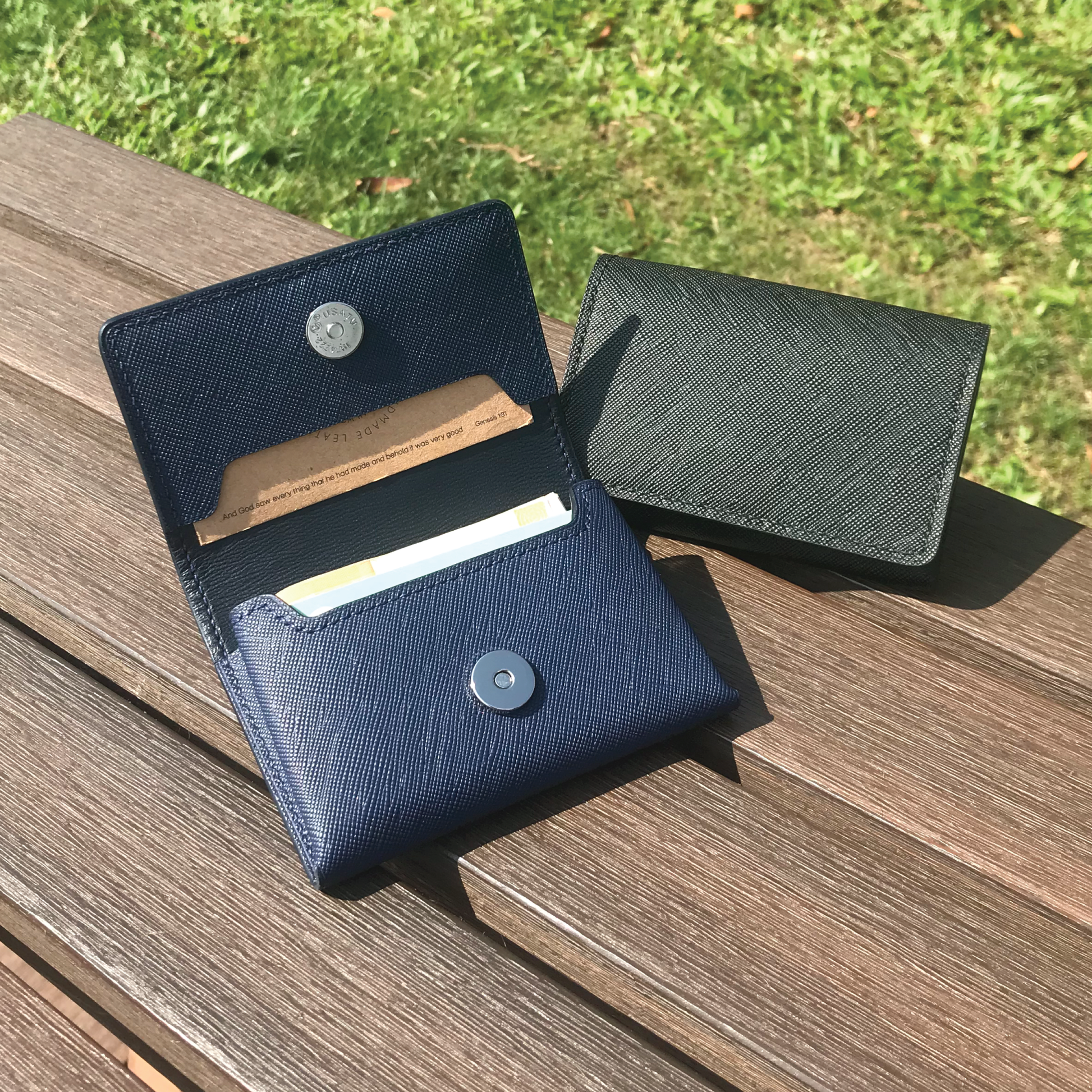 Two small wallets, one blue and one black, on a wooden surface with grass in the background.